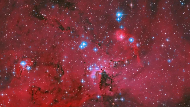NASA’s Hubble captures a crimson stellar nursery sparkling with blue and white stars